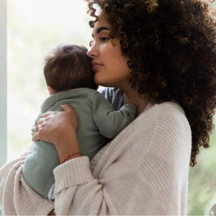 Tired mother holding her baby close during a quiet moment at home, reflecting the emotional side of caring for a colicky infant in New Zealand.